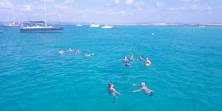 Een groep mensen geniet van een frisse duik in de zee. Er zijn boten in de verte.